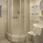 Badezimmer mit Dusche, Waschbecken und Toilette. Weiße Fliesen und grüne Seifenflaschen.