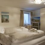 Schlafzimmer mit Bett, TV und Kleiderschrank. Fenster mit Vorhängen. Wandbild und Lampen.