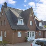 Ein rotes Backsteinhaus mit dunklem Dach und weißen Fenstern. Vor dem Haus steht ein Auto.
