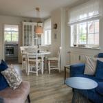 Wohn- und Essbereich mit blauem Sofa, runder Tisch und weißen Stühlen.