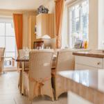 Essbereich mit Esstisch, Stühlen und Fenstern. Küche mit Arbeitsplatte und Schränken.