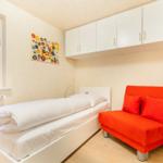 Ein Schlafzimmer mit weißem Bett, rotem Sofa und weißen Schränken an der Wand.