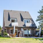 Haus mit Dachterrasse, Garten und Liegestühlen. Außenbereich mit Tischen und Sonnenschirmen.