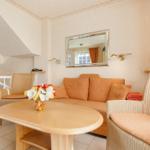 Wohnzimmer mit Sofa, Sessel und Tisch. Wandspiegel und Fenster mit Vorhängen.