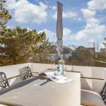Terrasse mit Tisch, Stühlen und Sonnenschirm. Blick auf Bäume und Himmel.