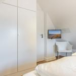 Schlafzimmer mit Bett, Kleiderschrank und Fernseher an der Wand.