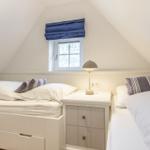 Zwei Betten mit weißen Bettwäsche und gestreiften Kissen. Zwischen den Betten steht ein Nachttisch mit Lampe.