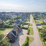 Aerial view of a coastal village with houses, gardens, and a road leading to the sea.