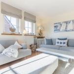 Wohnzimmer mit zwei grauen Sofas, Tisch und Wandbild mit Segelbooten.