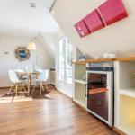 Esszimmer mit Tisch, Stühlen und Kühlschrank. Holzboden und Fenster.