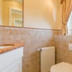 Bathroom with sink, mirror, radiator, and toilet. Window with curtain and plant.
