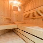 Sauna with wooden bench, wooden bucket, and thermometer on the wall.