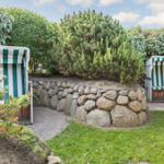 Two beach chairs with green-white fabric stand in the garden next to stone wall and grass.