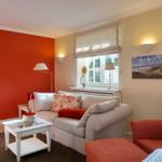 Living room with sofa, armchair, and window. Wall in red, furniture in white and red.