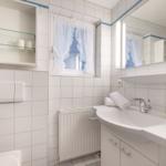 Badezimmer mit Waschbecken, Spiegel und Fenster mit weißen Vorhängen.