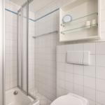 Badezimmer mit Dusche, Toilette und Aufbewahrungskasten an der Wand.