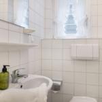 Badezimmer mit Waschbecken, Spiegel und Fenster mit weißen Vorhängen.