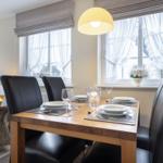 Esszimmer mit Holztisch, schwarzen Stühlen und Fenstern mit weißen Vorhängen.