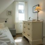 Bedroom with sloped ceiling, bed, dresser, and window with curtains.