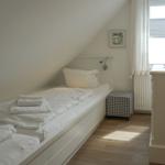 A bedroom with sloped ceiling, bed, dresser, and window.