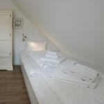Bedroom with double bed, white wardrobe, and wooden floor.