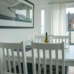 Dining area with white table and chairs, window overlooking balcony and house.