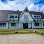 Modern white house with balconies and gable roof. Lawn with stones and paved area.