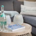 Runder Tisch mit Flasche, Gläsern und Buch vor grauem Sofa.