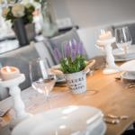 Gedeckter Esstisch mit Kerzen, Blumen und Geschirr.