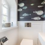 Badezimmer mit Fischmotiv-Wand, Fenster, Waschbecken und Toilette.