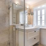 Badezimmer mit Dusche, Waschbecken und Fenster.