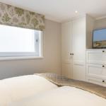 Schlafzimmer mit Bett, Schrank und Fernseher an der Wand.