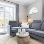 Ein Wohnzimmer mit grauem Sofa, Holzboden und Fenster zur Terrasse.
