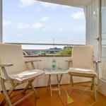 Balcony with two chairs and a table for two. View over rooftops and sky.