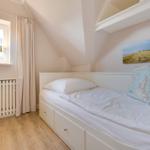Schlafzimmer mit Dachschrägen, weißem Bett und Holzboden. Fenster mit Vorhang und Wandbild.