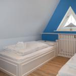 Zimmer mit zwei Betten, blauer Wand und Dreiecksfenster