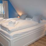 Schlafzimmer mit Doppelbett, Fenster und Nachttisch.