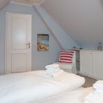 Schlafzimmer mit Dachschrägen, Bett, Stuhl und Schrank.