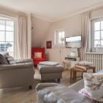 Wohnzimmer mit Sofa, Sessel und TV. Große Fenster und Holzboden.
