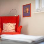 Rotes Sessel mit Kissen, Wandbild und Fensterbank mit Lampen.