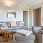 Wohnzimmer mit Sofa, Sitzbank und Holztischen. Wandbild und Stehlampe sichtbar.