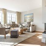 Living room with sofa, armchair, fireplace, and large windows.