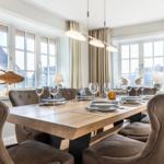 Dining room with wooden table, chairs, and windows with curtains.