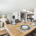Dining room with set table, living area, and staircase in background.