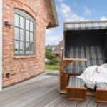 Deck with wicker lounge chair and wooden floor beside brick house