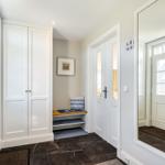 Entrance with shoe cabinet, bench, and mirror. White doors and dark tiles.