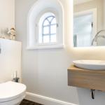 Bathroom with sink, toilet, and arched window.