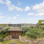 Green rooftop garden with stone walls and view of beach area.