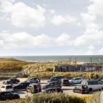 From the window, you see a parking lot with cars and the sea.