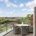 Terrace with table and chairs, view of beach and green areas.